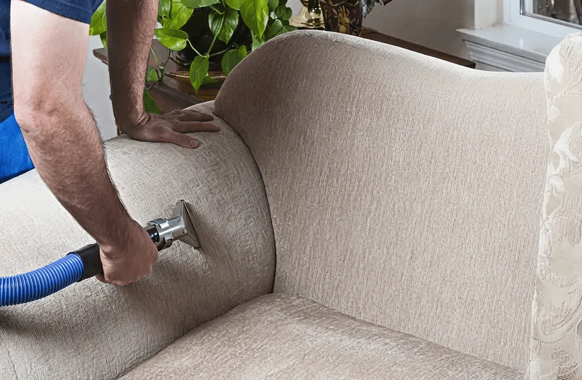 Professional upholstery cleaner deep-cleaning a fabric sofa with a handheld extraction tool and hose, Wichita, KS.